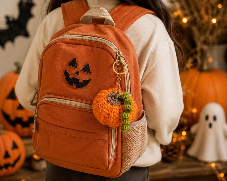 Puede incluir: Mochila naranja con un aplique de cara de calabaza. Un llavero de calabaza de ganchillo cuelga de la cremallera. La mochila tiene un bolsillo frontal y un bolsillo lateral de malla. Tema de Halloween.