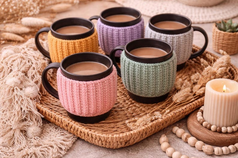 May include: A set of three ceramic mugs with a speckled, cream-colored glaze. Each mug features a different hand-painted floral design in shades of blue, green, and yellow. The mugs have a simple, rounded shape and a comfortable handle.