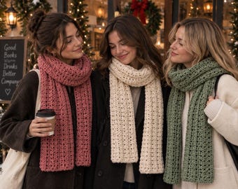 May include: Three long, chunky knit scarves in solid colors of dusty rose, cream, and sage green. Each scarf features a textured, repeating vertical stitch pattern with a soft, thick appearance, draped loosely around the neck over winter coats.