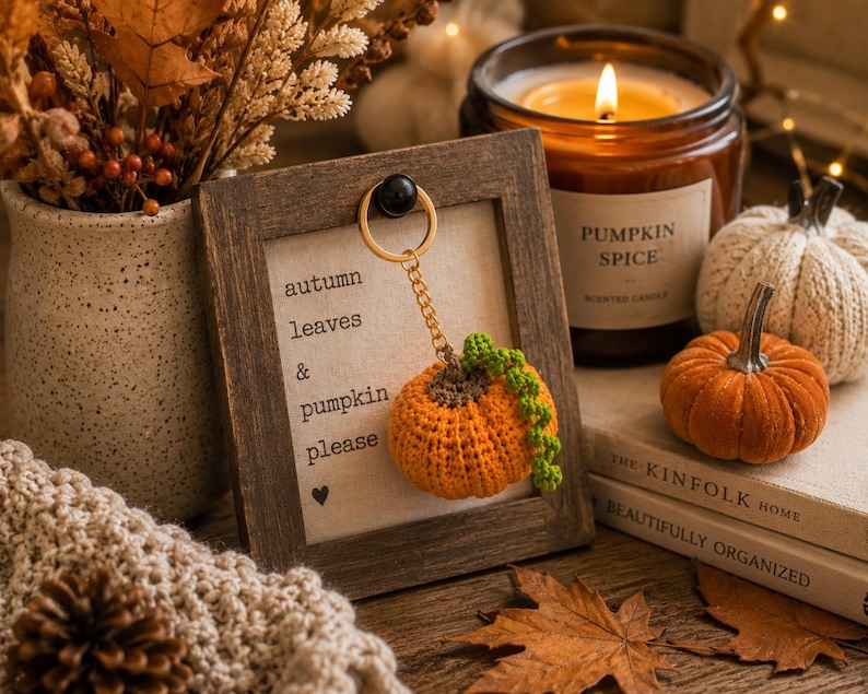 Puede incluir: Naturaleza muerta con tem&aacute;tica oto&ntilde;al con un llavero de calabaza de ganchillo, una vela de especias de calabaza encendida y calabazas decorativas. El texto enmarcado dice "autumn leaves & pumpkin please".