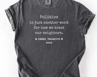 Op de afbeelding: Donkergrijs t-shirt met de tekst "Politics is just another word for how we treat our neighbors." De tekst bevat ook "JAMES TALARICO 2026" in het wit. Het shirt is opgevouwen en het woord "PEPPER" staat in een banner.