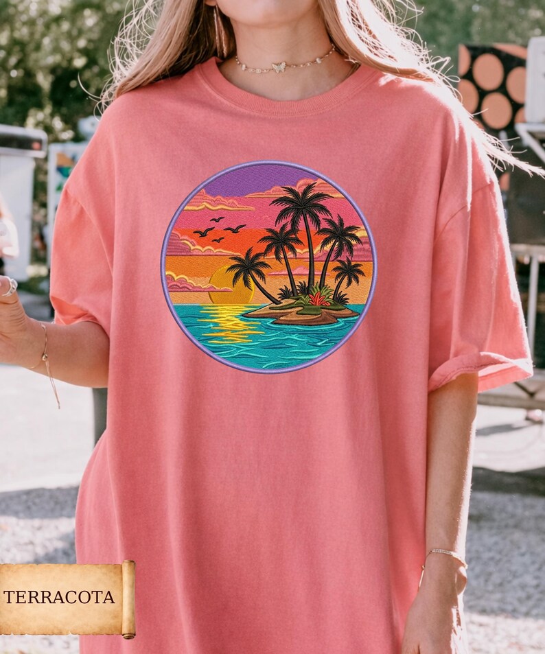 May include: Terracotta-colored t-shirt featuring a circular graphic of a tropical island scene. The design includes palm trees, a sunset, and ocean waves. The shirt has short sleeves and a relaxed fit.