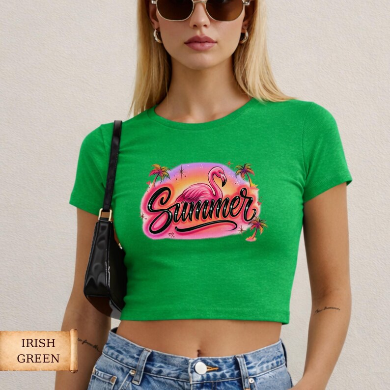 K&ouml;nnte beinhalten: Ein gr&uuml;nes Crop-Top mit einer Grafik, die einen rosa Flamingo, das Wort "Summer" in Schreibschrift und Palmen zeigt. Das Shirt ist in einem leuchtenden Gr&uuml;nton gehalten und hat kurze &Auml;rmel.