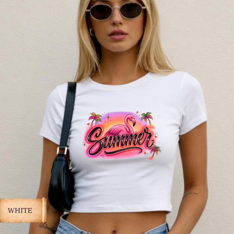 White baby tee with a tropical pink “Summer” graphic featuring a flamingo, palm trees, sunset colors, and sparkles in a retro Y2K aesthetic style