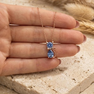 Puede incluir: Un collar con colgante de gato en oro rosa con piedras preciosas azules. La cabeza y el cuerpo del gato están representados por piedras preciosas azules redondas y en forma de pera. El collar tiene una cadena delicada.