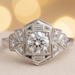 May include: A silver engagement ring with a large, round, clear diamond center stone. The ring features a geometric design with smaller diamonds and baguette-cut stones. The ring is set on a white background.