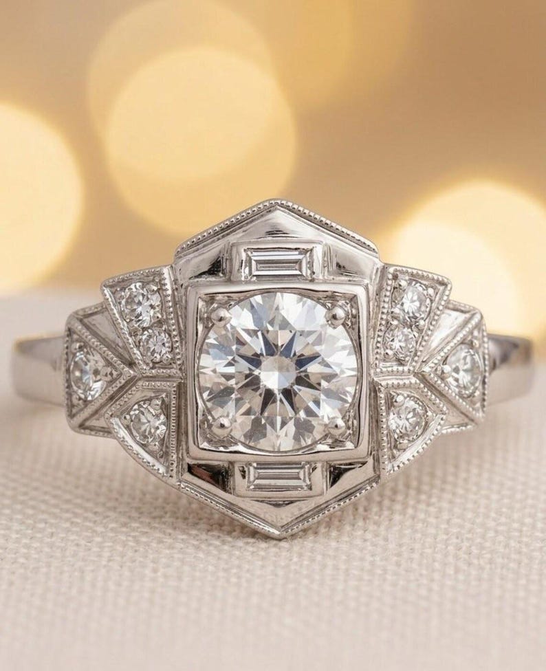 May include: A silver engagement ring with a large, round, clear diamond center stone. The ring features a geometric design with smaller diamonds and baguette-cut stones. The ring is set on a white background.