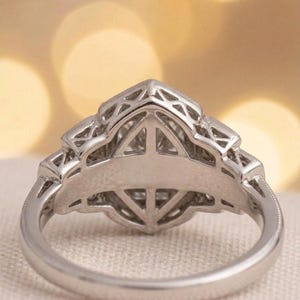 May include: Close-up of a silver ring with an intricate geometric design. The ring features a central setting with a triangular shape, surrounded by detailed filigree work. The band has a smooth, polished finish.