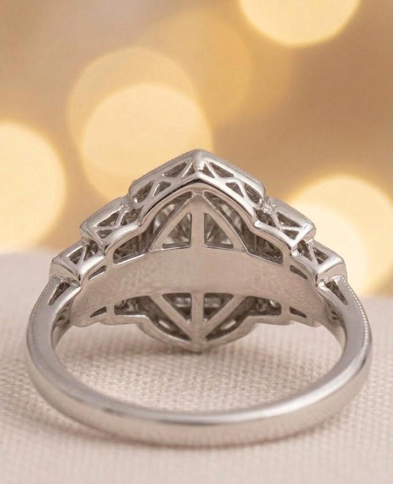 May include: Close-up of a silver ring with an intricate geometric design. The ring features a central setting with a triangular shape, surrounded by detailed filigree work. The band has a smooth, polished finish.