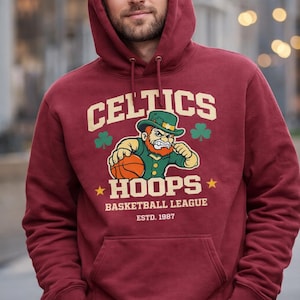 May include: Maroon hoodie with the text "CELTICS HOOPS BASKETBALL LEAGUE ESTD. 1987" and a cartoon leprechaun holding a basketball. The hoodie has a drawstring hood and a front pocket.