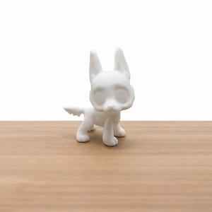 Könnte beinhalten: Kleine, weiße Keramikfigur eines Hundes mit aufrechten Ohren und einem Schwanz. Der Hund steht auf allen Vieren, mit glatter, matter Oberfläche. Der Hintergrund ist schlicht weiß, und die Figur steht auf einer Holzoberfläche.