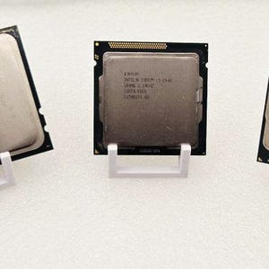 Peut inclure: Trois processeurs d'ordinateur présentés sur des supports blancs. Les processeurs ont une forme rectangulaire avec une surface métallique et des bordures noires. Chaque processeur a un design et un texte différents.