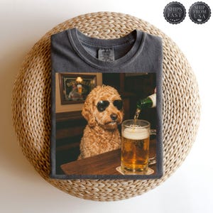 May include: Dark grey t-shirt with a humorous image of a dog wearing sunglasses, sitting at a bar, and beer being poured into a pint glass. The image includes a framed sign that reads "Bing Beer".