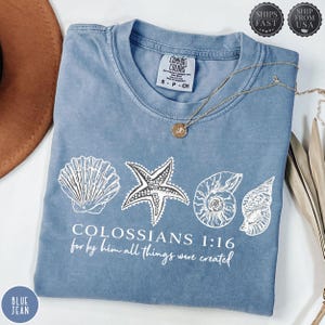 Könnte beinhalten: Ein blaues Comfort Colors T-Shirt mit weißen Muschelgrafiken und dem Text "COLOSSIANS 1:16 for by him all things were created." Eine goldene Halskette mit Anhänger liegt auf dem Shirt.