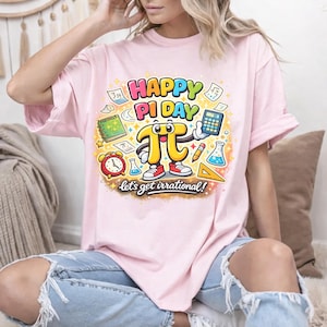 以下が含まれることがあります： ピンク色のTシャツ。カラフルなグラフィックで円周率の日を祝っています。「HAPPY PI DAY」と「let's get irrational!」の文字、数学記号、漫画のPiのキャラクターが描かれています。