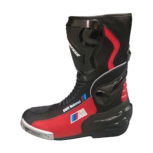 Può includere: Uno stivale da moto nero, rosso e bianco con il logo Dainese sulla parte superiore e sullo slider in punta. Il lato mostra la scritta BMW Motorrad e il logo M con strisce blu, viola e rosse. Presenta una protezione rigida per tallone e caviglia.