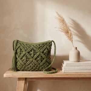 May include: An olive green macrame crossbody bag featuring a diamond-patterned knotted design, a zipper closure, and a long braided strap. A decorative tassel hangs from the side of the bag, which is constructed from thick cord.