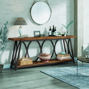 May include: A rustic console table with a dark brown wooden top and a lower shelf. The table has a black metal frame with oval accents. A lamp, mirror, and decorative items are displayed on the table.