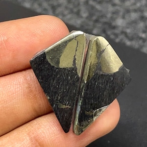 May include: A geometric mineral specimen featuring a combination of metallic gold-colored pyrite and a matte black, textured material. The piece has a distinct angular shape with a central vertical seam dividing the two contrasting surfaces.