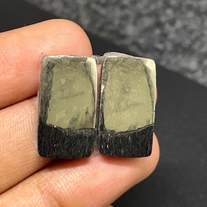 May include: Two rectangular cabochons featuring a dual-tone appearance with a metallic, brass-colored upper section and a textured, matte black lower section. The stones have a flat surface and straight edges, displaying a distinct contrast between the reflective gold-toned mineral and the dark, fibrous-looking base material.