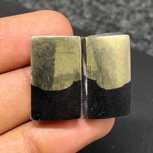 May include: Two rectangular stones featuring a dual-tone appearance. The top portion of each stone is a metallic, reflective gold color with a crystalline texture, while the bottom portion is a solid, matte black material with a smooth surface.