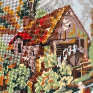 May include: A detailed needlepoint tapestry depicting a rustic barn scene. The artwork features a brown barn with a red roof, surrounded by green and brown foliage. The tapestry is created with various shades of thread, showcasing a textured, handcrafted appearance.