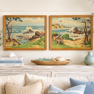 May include: Two rectangular framed landscape paintings depicting a coastal scene with rocky shores, crashing waves, and a lighthouse. The artwork features a palette of blue, green, and brown tones, encased in light wood frames, displayed side by side.