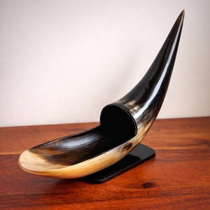 May include: A white ceramic mug with a black handle and the text "But First, Coffee" in a black, bold font. The mug is sitting on a wooden surface. The mug is approximately 4 inches tall.