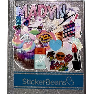 May include: A glittery silver notebook with the name "MADYN" in large, colorful letters. The cover is decorated with various stickers, including a disco ball, ice cream, lipstick, and the text "Camp Rocks". The bottom of the notebook has the text "StickerBeans".