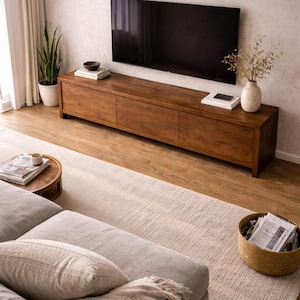 K&ouml;nnte beinhalten: Ein langes, rechteckiges Medienboard aus Holz mit drei Frontt&uuml;ren und einer glatten, mittelbraunen Holzmaserung. Das M&ouml;belst&uuml;ck ist horizontal an einer Wand unter einem gro&szlig;en Flachbildfernseher positioniert.