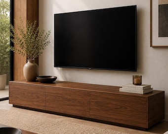 以下が含まれることがあります： 壁掛け式の薄型テレビの下に配置された、3つの扉を持つ長方形の木製メディアコンソール。このコンソールはダークウッドの木目調仕上げで、低い台座の上に設置されており、花瓶、ボウル、本が置かれています。