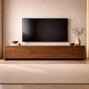 以下が含まれることがあります： モダンなリビングルーム。大きな黒いテレビが低い木製のメディアコンソールの上に設置されています。コンソールには3つの引き出しがあり、装飾的なボウルと緑のある花瓶が両側にあります。ニュートラルな色合いのラグと木製のフローリングが空間を完成させています。コンソールは約180cmの長さです。