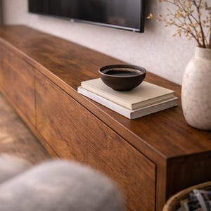 K&ouml;nnte beinhalten: Ein langes, rechteckiges Medienboard aus Holz mit dunkelbrauner Holzmaserung. Darauf befinden sich zwei cremefarbene B&uuml;cher, eine kleine dunkelbraune Keramikschale und eine gesprenkelte, cremewei&szlig;e Vase mit getrockneten Zweigen.