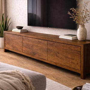 K&ouml;nnte beinhalten: Ein langes, rechteckiges Medienboard aus dunkelbraunem Holz mit sichtbarer Maserung. Das M&ouml;belst&uuml;ck verf&uuml;gt &uuml;ber drei flache Schrankt&uuml;ren und eine glatte Oberfl&auml;che, die eine stabile Basis f&uuml;r einen gro&szlig;en, wandmontierten Fernseher bietet.