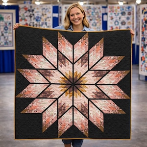 May include: A handmade quilt featuring a large starburst design. The star is composed of various floral patterned fabrics in shades of pink, peach, and brown, set against a black background. The quilt is held up by a person.