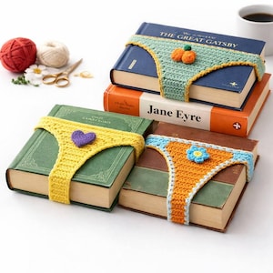 Puede incluir: Libros con cubiertas de ganchillo en forma de ropa interior en amarillo, naranja y verde. Las cubiertas presentan decoraciones de corazón, flores y calabazas. Se ven ovillos de lana y tijeras en el fondo, sugiriendo un proyecto artesanal.