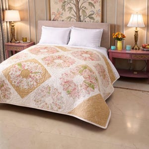 May include: A floral quilt featuring a repeating pattern of pink and white flowers on a cream backdrop. The quilt has a gold border and is on a bed with white pillows. The room has a vintage aesthetic with matching bedside tables and lamps.