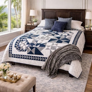 Peut inclure: Un lit avec une tête de lit en bois foncé est recouvert d'une courtepointe à motifs géométriques bleu marine, gris et blancs. Des coussins décoratifs bleus et une couverture grise ajoutent de la texture. Deux tables de chevet avec lampes encadrent le lit.