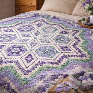 May include: A handmade quilt featuring a star pattern in purple, green, and white hues. The quilt is displayed on a bed, with sewing supplies and flowers. The quilt measures approximately 203 cm by 229 cm.