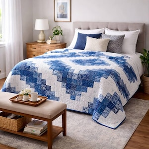 Könnte beinhalten: Eine blau-weiße Steppdecke mit geometrischem Muster bedeckt ein Bett. Die Steppdecke hat ein Patchwork-Design mit verschiedenen Blau- und Weißtönen. Das Bett ist mit Kissen und einer Bank am Fußende des Bettes ausgestattet.