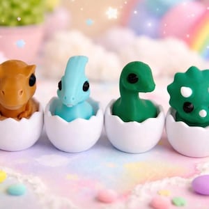Puede incluir: Cuatro figuras de dinosaurios coloridos, en naranja, azul, verde y verde oscuro, cada uno dentro de una cáscara de huevo blanca. El fondo presenta un arcoíris pastel y estrellas, con elementos decorativos.