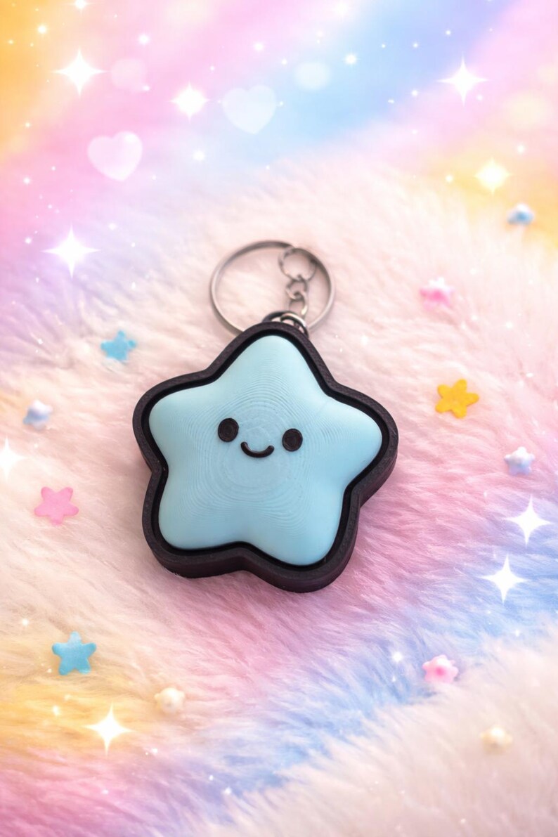 May include: A light blue star-shaped keychain with a smiling face and a dark brown border. The keychain is attached to a silver metal ring. The background is a soft, colorful blend of pink, blue, and yellow.