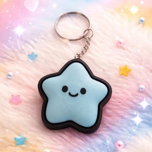 May include: A light blue star-shaped keychain with a smiling face and a black border. The keychain has a silver ring and chain. The background is a soft, fluffy material with pastel colors and star-shaped decorations.