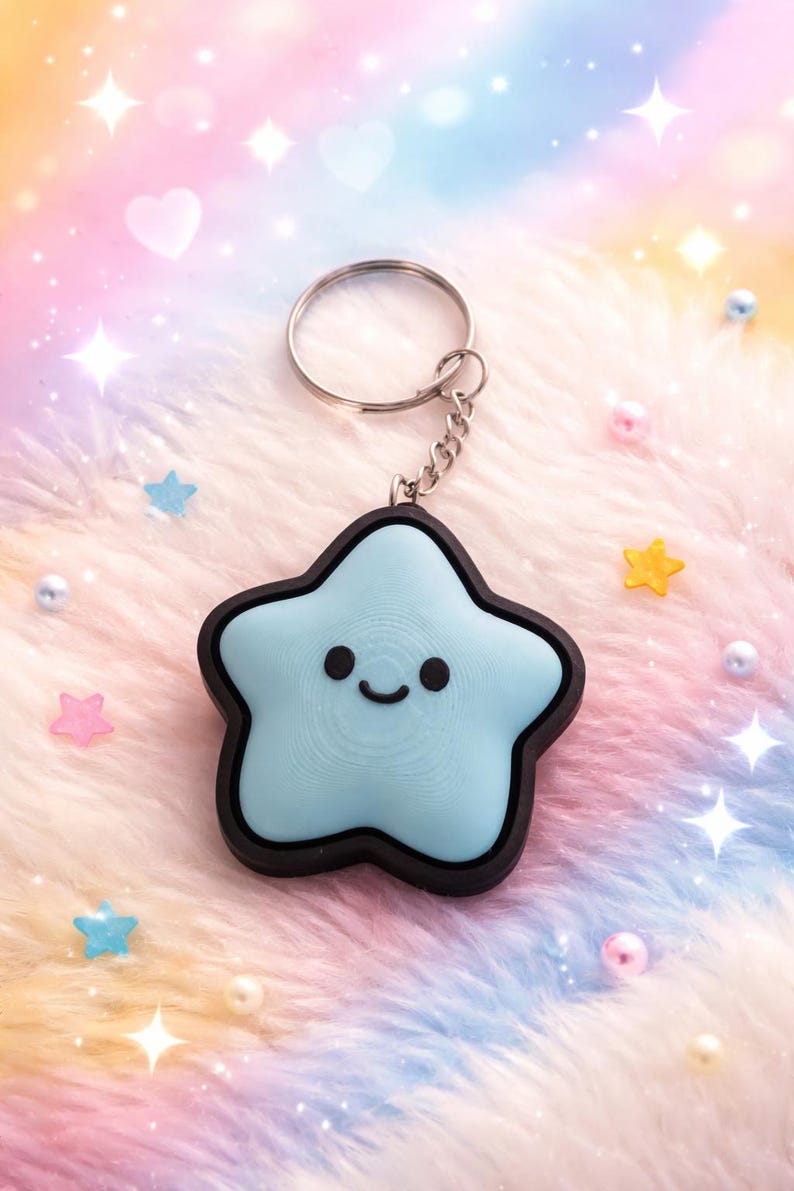 May include: A light blue star-shaped keychain with a smiling face and a black border. The keychain has a silver ring and chain. The background is a soft, fluffy material with pastel colors and star-shaped decorations.