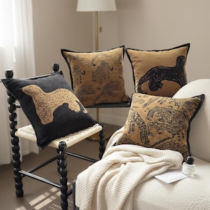 May include: Four decorative cushions with animal designs. Two cushions feature a tan leopard pattern on a tan background. One cushion has a black background with a tan leopard. The fourth cushion has a tan background with a black animal design.