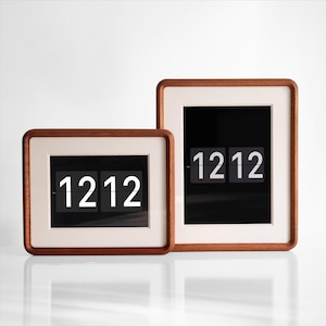 Puede incluir: Dos relojes de solapa rectangulares con marcos de madera, ambos mostrando "1212". Los relojes tienen un interior de color claro y un fondo oscuro para los números. Los marcos son de color marrón cálido, sobre un fondo blanco.