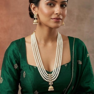May include: A woman wearing a green blouse and matching green shawl, adorned with a multi-strand pearl necklace and gold earrings. The blouse has gold embroidery and a square neckline. A gold watch is on her wrist.