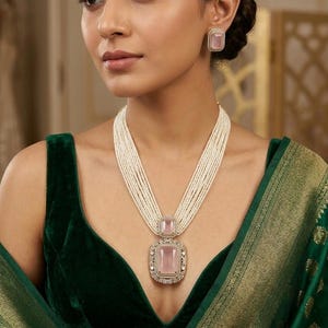 May include: A woman wearing a multi-strand pearl necklace with a large, rectangular pink gemstone pendant and matching earrings. The jewelry is set in a silver-toned metal. She is wearing a dark green velvet top and a green silk shawl.