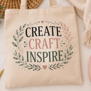 Peut inclure: Un sac fourre-tout en toile beige avec le texte noir et rose "CREATE CRAFT INSPIRE" centré à l'intérieur d'une couronne décorative de feuilles vertes et roses et de petits cœurs. Le motif est imprimé sur le devant du sac en tissu.