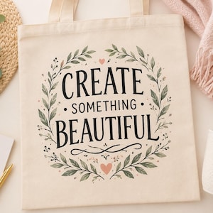 Peut inclure: Un sac fourre-tout en toile couleur crème avec le texte noir "CREATE SOMETHING BEAUTIFUL" centré à l'intérieur d'une couronne de feuilles vertes et de petits cœurs roses. Le motif est imprimé sur le devant du sac avec deux anses solides.